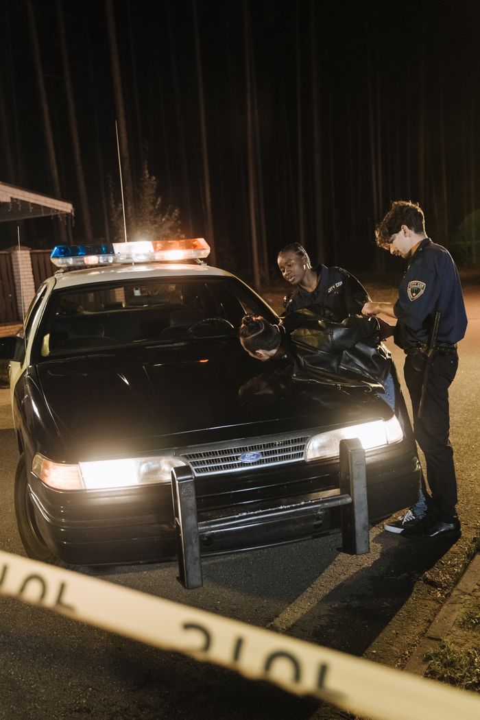 Nighttime arrest scene with police officers detaining a suspect by a patrol car.